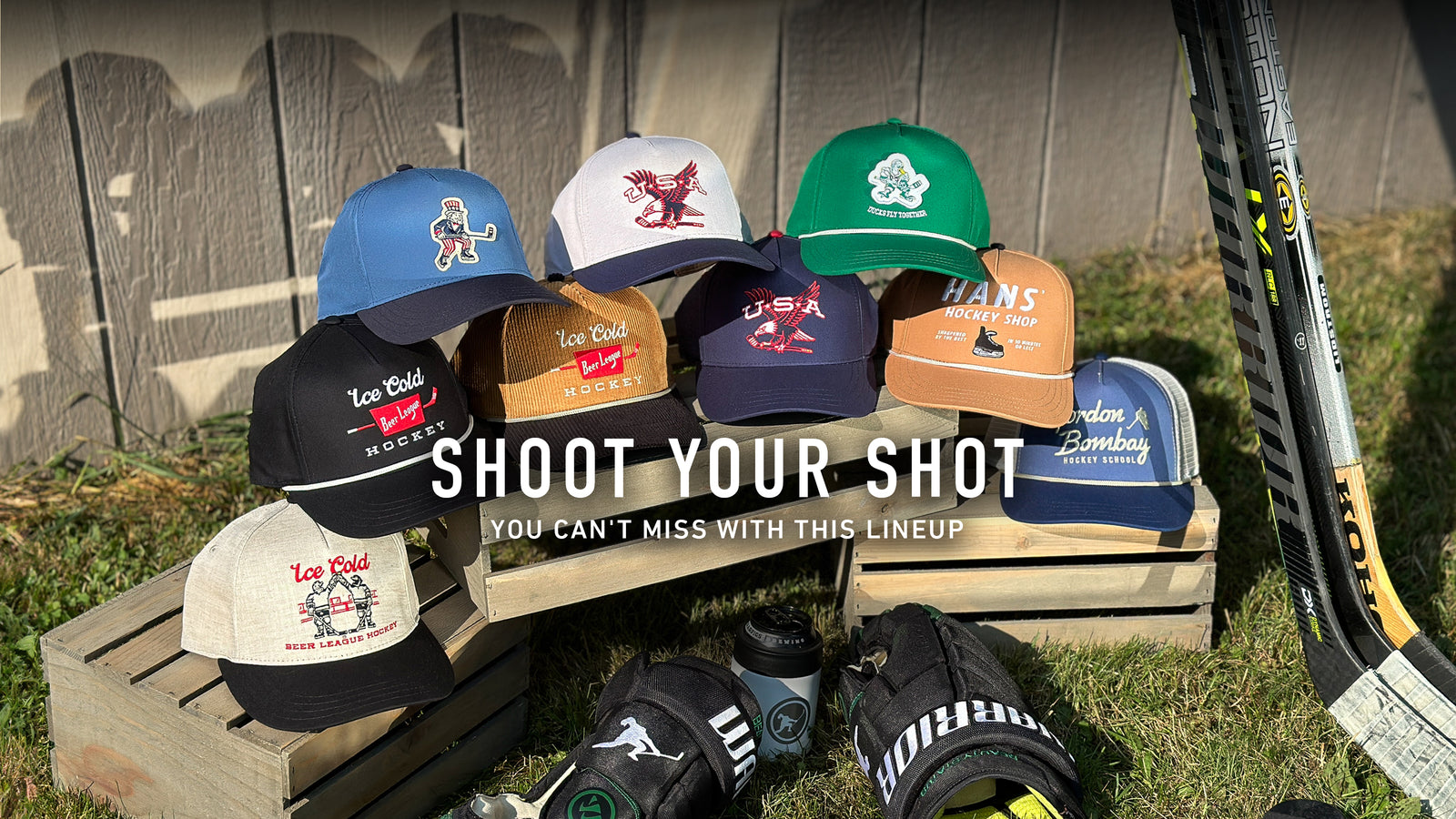 A lineup of Beauty Status hockey hats on a wooden crate next to hockey gloves and a stick